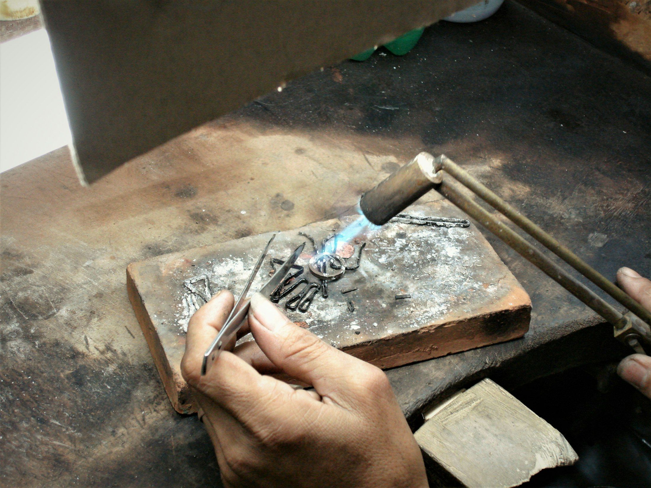 A silversmith's hands engraving a piece of silver at a workbench