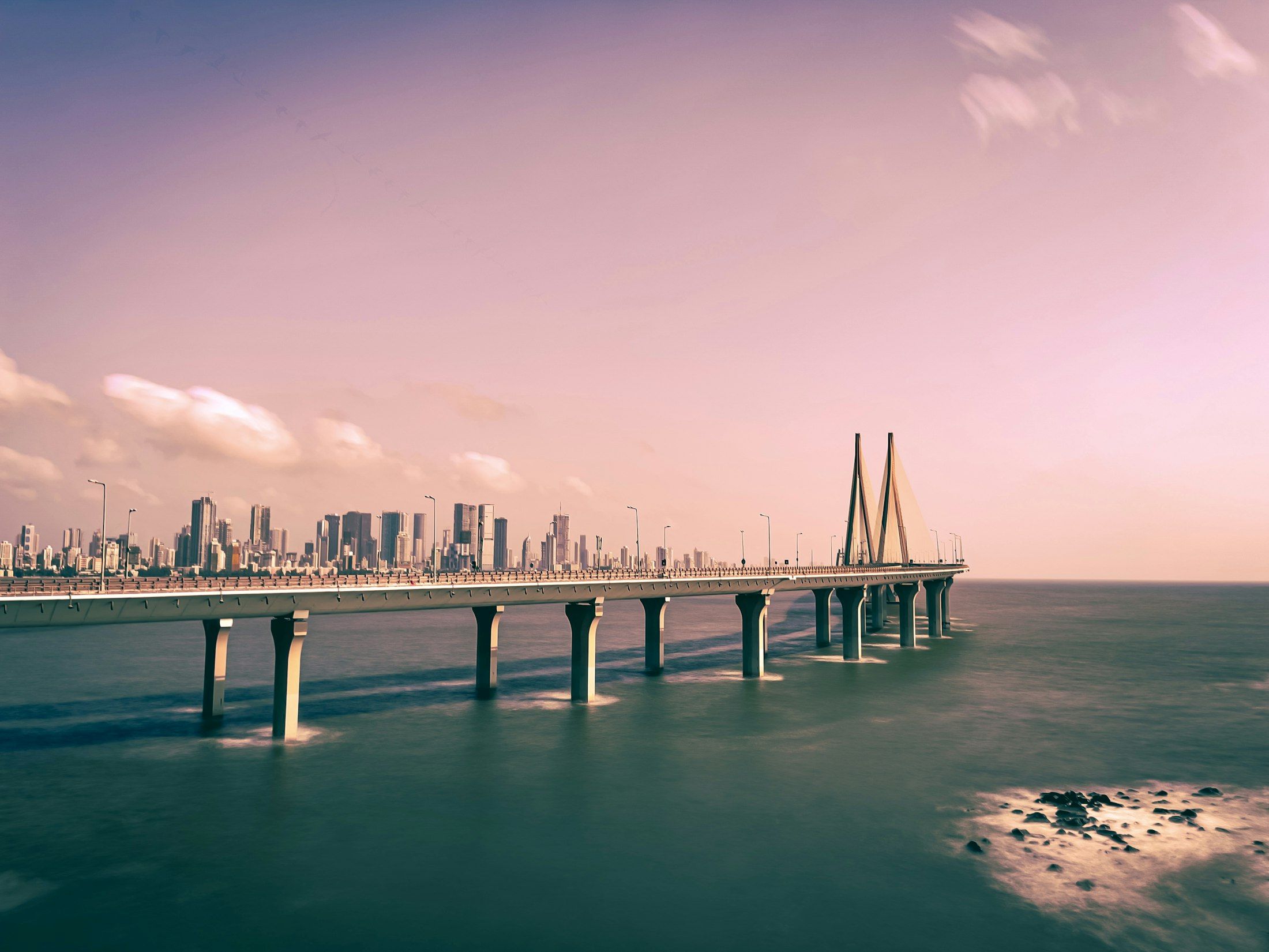 Eine lange Brücke über das Wasser in Richtung einer Stadtsilhouette in der Morgendämmerung