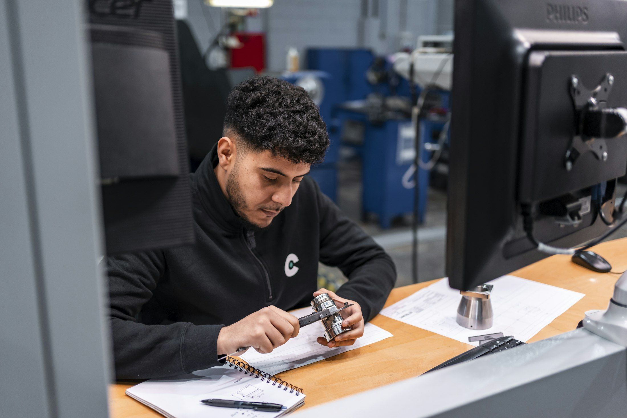 Ein Techniker misst sorgfältig ein Metallbauteil am Arbeitsplatz